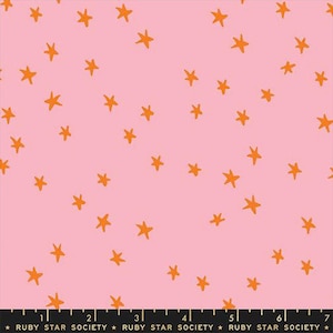 Può includere: Tessuto rosa con un motivo di stelle arancioni. Le stelle sono sparse sulla superficie. La parte inferiore del tessuto ha un righello con il testo "RUBY STAR SOCIETY".