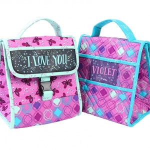 Può includere: Due borse da pranzo trapuntate rosa con bordi blu. Una borsa ha una finestra trasparente con la parola "VIOLET" stampata su di essa. L'altra borsa ha una finestra nera con le parole "I LOVE YOU" stampate su di essa.