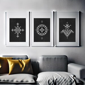 以下が含まれることがあります： 黒地に幾何学模様が描かれた白黒の額装されたプリントが3枚。プリントは灰色の壁に掛けられており、灰色のソファの上に黄色のクッションが置かれている。