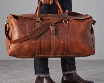 May include: A large brown leather duffel bag featuring two top handles, a detachable shoulder strap with a padded section, and brass-toned metal hardware. The bag has vertical leather straps with buckles and reinforced rivets.