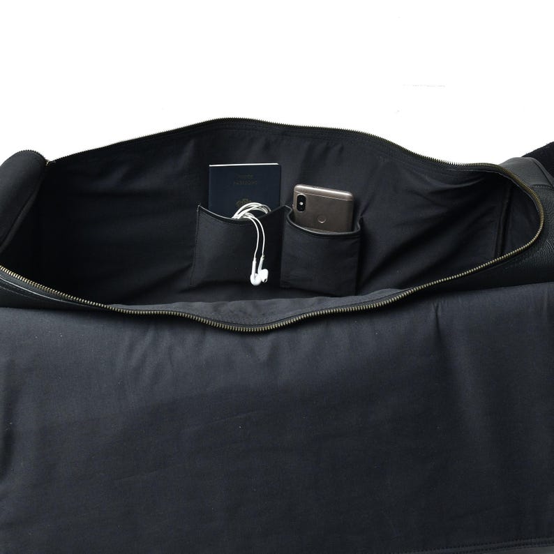 Open interior of a black duffle bag showing a dark lining with two slip pockets containing a passport and a smartphone with tangled wired earphones.