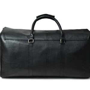 Front view of a black leather duffle bag resting on a white background with two top carrying handles and a detachable shoulder strap.