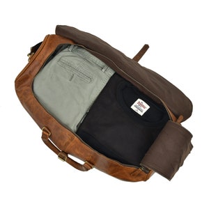 May include: A brown leather duffel bag with a zippered opening. The bag is open and contains a pair of khaki pants and a black t-shirt with a white label that reads "The Original Buffalo" and "Since 1973".