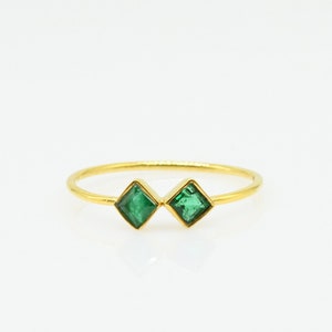 May include: A delicate gold ring with two emerald green square-shaped gemstones.
