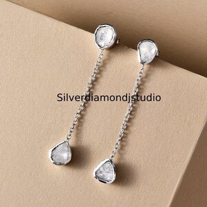 May include: A pair of silver dangle earrings with a rough diamond-shaped stone at the top and a smaller diamond-shaped stone at the bottom of each earring.