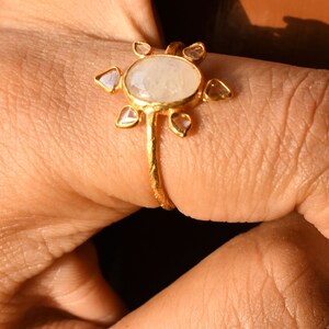 K&ouml;nnte beinhalten: Ein goldener Ring mit einem gro&szlig;en ovalen Mondstein und kleineren diamantf&ouml;rmigen Steinen, die darum herumgesetzt sind.