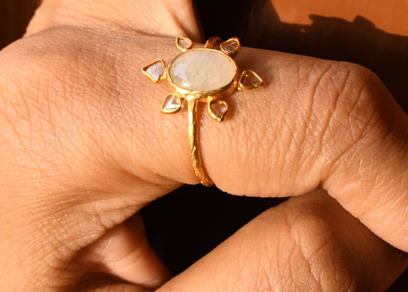 K&ouml;nnte beinhalten: Ein goldener Ring mit einem gro&szlig;en ovalen Mondstein und kleineren diamantf&ouml;rmigen Steinen, die darum herumgesetzt sind.