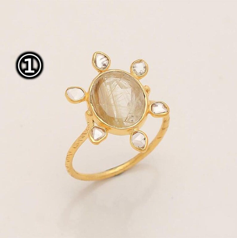 K&ouml;nnte beinhalten: Ein goldener Ring mit einem gro&szlig;en, ovalen, klaren Edelstein, der von kleineren, klaren Edelsteinen umgeben ist. Der Ring hat eine strukturierte Band.
