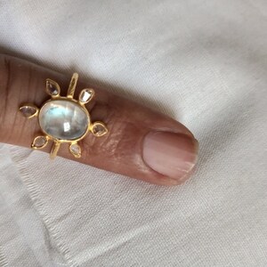 K&ouml;nnte beinhalten: Ein goldener Ring mit einem gro&szlig;en ovalen Mondstein und kleineren diamantf&ouml;rmigen Steinen darum herum.