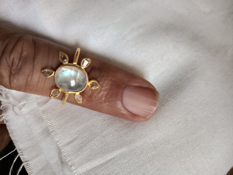 K&ouml;nnte beinhalten: Ein goldener Ring mit einem gro&szlig;en ovalen Mondstein und kleineren diamantf&ouml;rmigen Steinen darum herum.