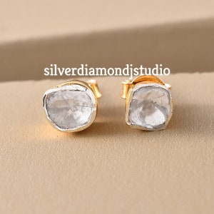 May include: A pair of silver earrings featuring a clear, faceted gemstone set in a gold setting. The earrings are small and delicate, and would make a lovely gift for a special occasion.