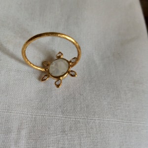 K&ouml;nnte beinhalten: Ein goldener Ring mit einem gro&szlig;en wei&szlig;en ovalen Edelstein, der von kleineren wei&szlig;en Edelsteinen umgeben ist.