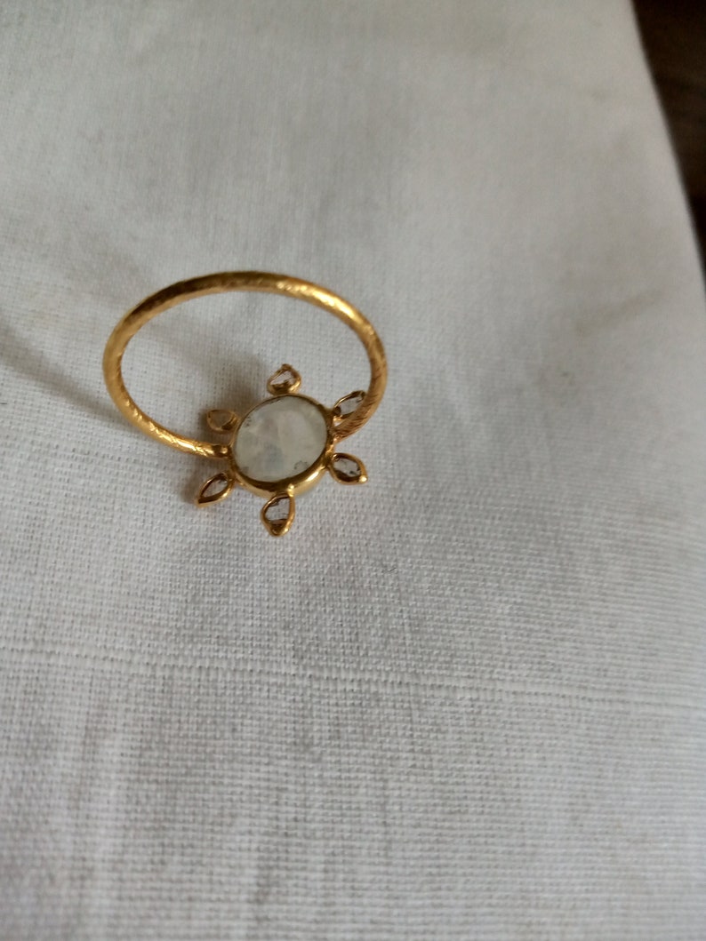 K&ouml;nnte beinhalten: Ein goldener Ring mit einem gro&szlig;en wei&szlig;en ovalen Edelstein, der von kleineren wei&szlig;en Edelsteinen umgeben ist.
