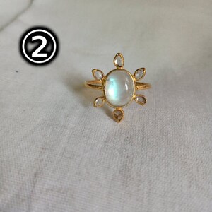 K&ouml;nnte beinhalten: Ein goldener Ring mit einem gro&szlig;en ovalen Mondstein und kleineren klaren Steinen, die in einem Sonnenstrahlenmuster darum herum angeordnet sind.