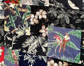 May include: A patchwork quilt made of various fabrics featuring tropical floral patterns in shades of red, white, black, and green.