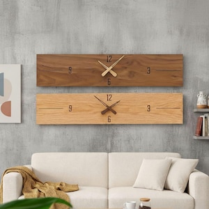 May include: Two rectangular wooden wall clocks. One is a dark brown color, the other is light brown. Each clock has a minimalist design with the numbers 3, 6, 9, and 12 marked. The clock hands are gold and brown.