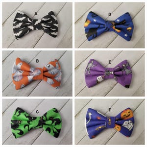 May include: Six bow ties labeled A through F with Halloween patterns. A has black bats on white. B has white ghosts on orange. C has black cats on green. D has black cats and stars on blue. E has skeletons on purple. F has pumpkins and bones on blue.