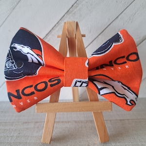 May include: Orange and black bow tie with the Denver Broncos logo and the words "Denver Broncos".