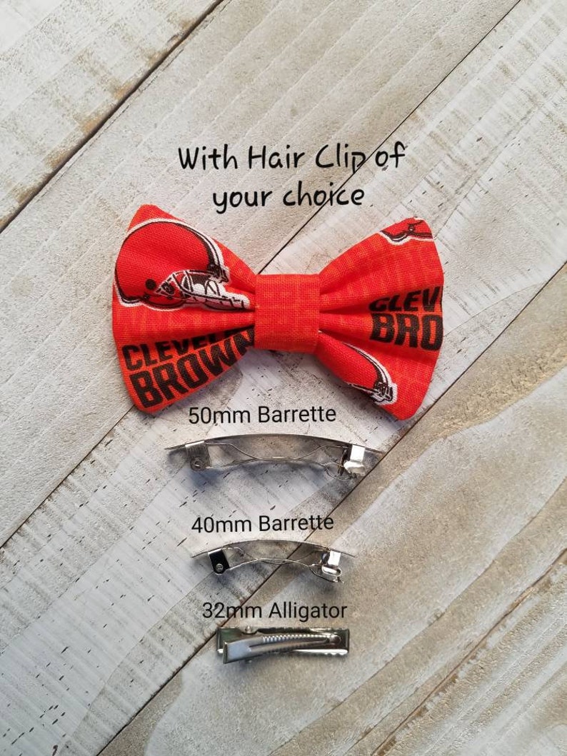 May include: Orange and brown bow tie hair clip with the text "CLEVELAND BROWN" and a football helmet design. The clip is available in three sizes: 50mm barrette, 40mm barrette, and 32mm alligator clip.