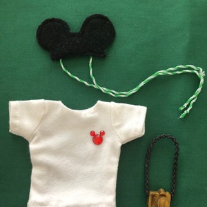 May include: A white t-shirt with a red Mickey Mouse head on the front, a black felt Mickey Mouse hat with white and green string, and a gold camera with a black chain.