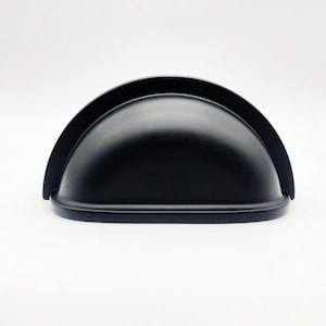 Peut inclure: Poignée de meuble noire en forme de demi-cercle arrondi.