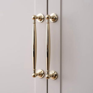 May include: Two gold cabinet pulls with round knobs on a white cabinet door.
