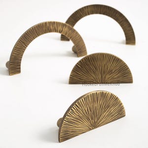 Op de afbeelding: Vier bronskleurige kastgrepen in een halfrond ontwerp. De grepen hebben een getextureerd, geribbeld oppervlak en een kleine, ronde knop aan het uiteinde. De grepen zijn geplaatst op een witte achtergrond.