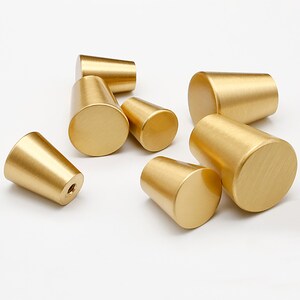 May include: A set of eight gold-toned cabinet knobs with a cone shape and a smooth, brushed finish.