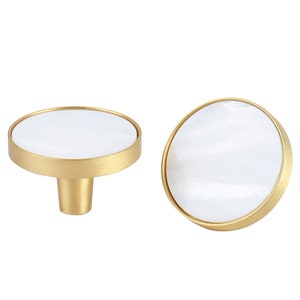 May include: Two round, gold-toned cabinet knobs with a white, pearlescent centre. The knobs have a smooth, polished finish.