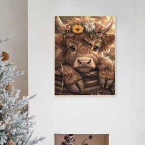 May include: A brown and white Highland cow with a flower crown resting its head on a wooden fence. The cow has a sweet expression and is looking directly at the viewer.