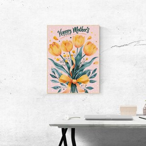 May include: A framed print with a pink background and white polka dots. The print features a bouquet of yellow tulips with green leaves and a yellow ribbon. The text "Happy Mother's" is written in a cursive font at the top of the print.