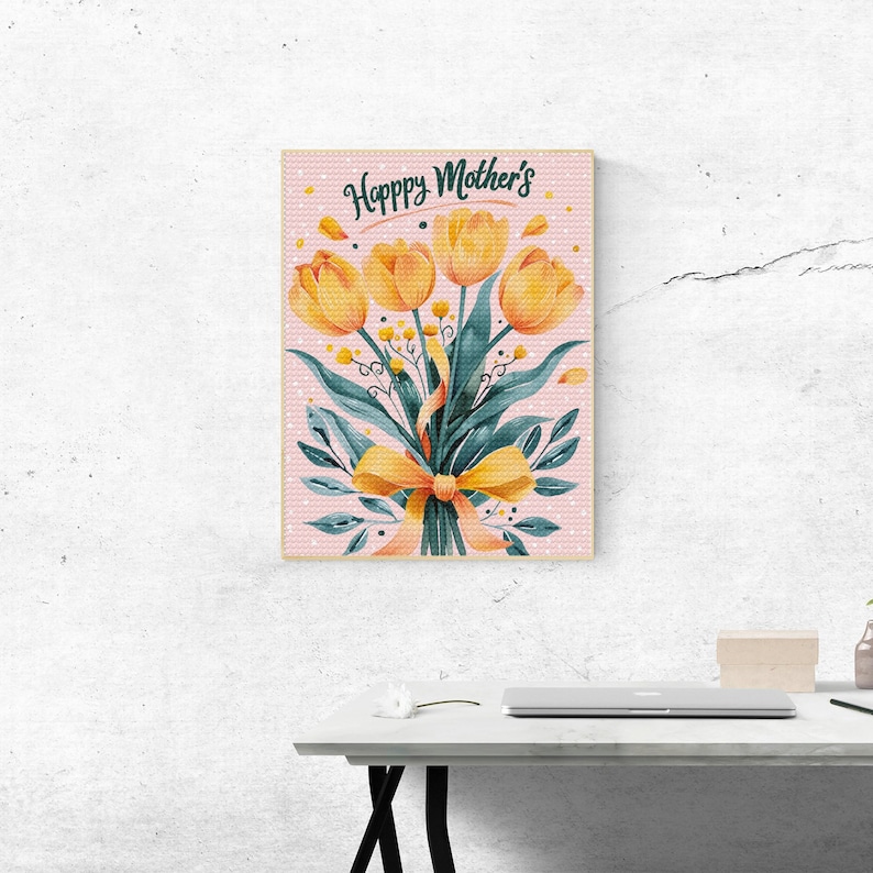 May include: A framed print with a pink background and white polka dots. The print features a bouquet of yellow tulips with green leaves and a yellow ribbon. The text "Happy Mother's" is written in a cursive font at the top of the print.
