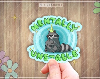 May include: A sticker featuring a cartoon raccoon wearing a party hat, with the words "Mentally Unstable" in green bubble letters. The raccoon is gray and white, set against a light blue background with a swirl design. The sticker is held by a hand.