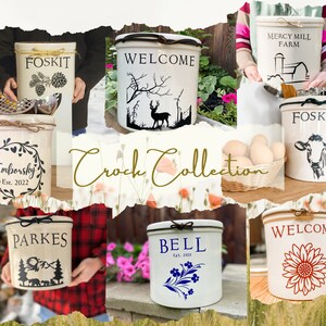 May include: A collection of white ceramic crocks with various designs and text. The crocks feature designs such as a deer, a sunflower, a cow, a mountain scene, and a floral pattern. The text on the crocks includes "Welcome", "Foskit", "Emborsky Est. 2022", "Parkes", "Bell Est. 2010", and "Mercy Mill Farm".