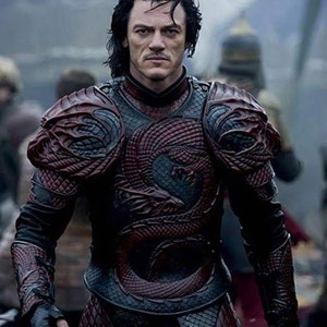 May include: A man wearing dark red and black dragon-scale armour with a detailed design. The armour has a high collar and covers the chest, shoulders, and arms.