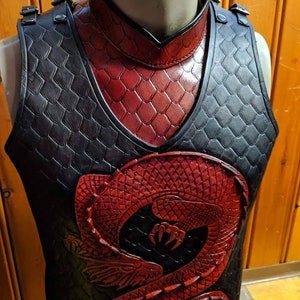 May include: A black leather vest featuring a red dragon design. The vest has a high collar and is decorated with a scale pattern.