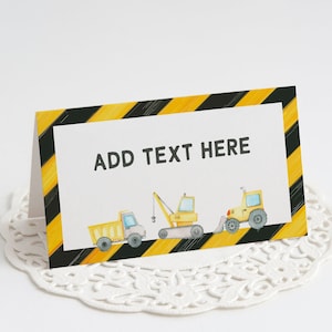 May include: A yellow and black construction themed place card with the text "ADD TEXT HERE" in black. The card features a yellow dump truck, a yellow excavator, and a yellow bulldozer.