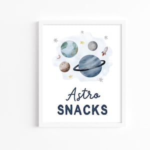 May include: A white framed print with a watercolor illustration of planets and a rocket ship. The text "Astro Snacks" is written in blue below the illustration.