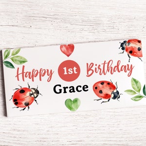 May include: A white card with red and green ladybirds, green leaves, and red hearts. The card says "Happy 1st Birthday Grace".
