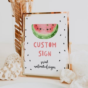 May include: A gold-framed sign with a white background and a cartoon watermelon illustration. The text on the sign reads "CUSTOM SIGN print unlimited signs".