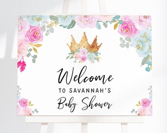 Puede incluir: Un cartel de bienvenida blanco con una corona dorada y detalles florales rosas y azules. El texto dice "Bienvenido al Baby Shower de Savannah".