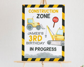Peut inclure: Une pancarte d'anniversaire de chantier jaune et noire avec le texte "Construction Zone", "James's 3rd Birthday", et "In Progress". La pancarte représente deux véhicules de chantier dessinés, un bulldozer et une excavatrice.