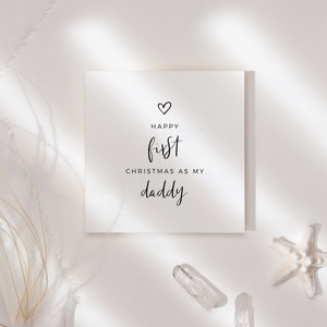 May include: A white card with black text that reads "Happy first Christmas as my daddy" with a small heart above the word "Happy".