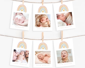 May include: Six baby milestone cards are displayed on a string with wooden clothespins. Each card features a photo of a baby and a rainbow graphic. The cards are labeled "Newborn", "One Month", "Two Months", "Three Months", "Four Months", and "Five Months".