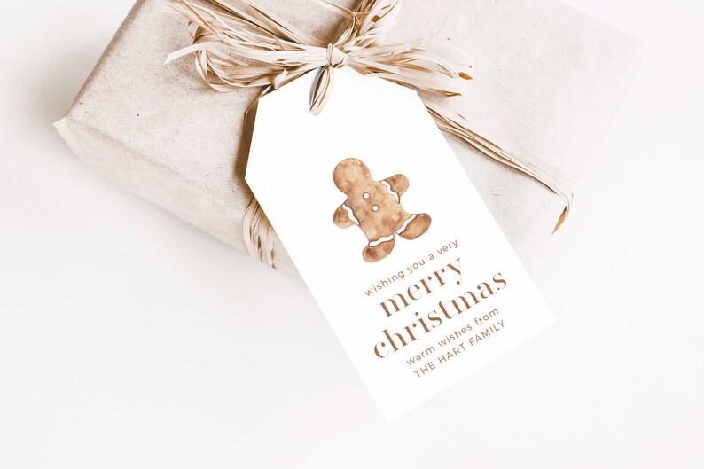 May include: A wrapped gift with a white tag featuring a watercolor gingerbread man. The tag reads "wishing you a very merry christmas" and "warm wishes from THE HART FAMILY". The gift is tied with raffia.