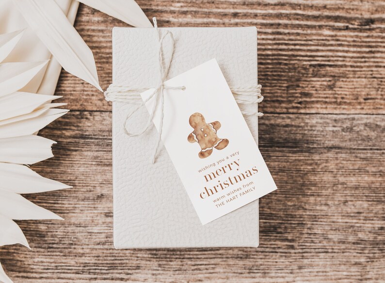May include: A wrapped gift box with a tag featuring a watercolor gingerbread man and the text "wishing you a very merry christmas". The gift is tied with twine and rests on a wooden surface.