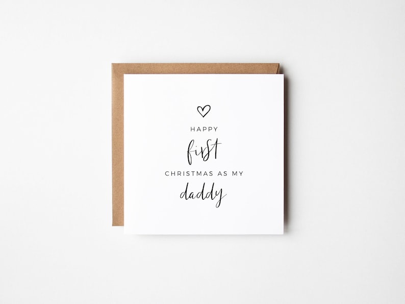 May include: A white card with black text that reads "Happy first Christmas as my daddy" with a small heart above the word "Happy".