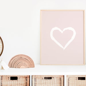 May include: A white heart drawn on a pink background in a wooden frame. The frame is on a white shelf with a wooden rainbow toy and a globe in the background.