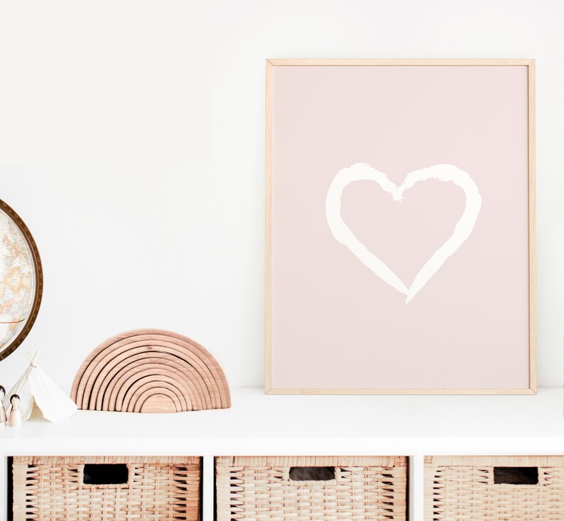 May include: A white heart drawn on a pink background in a wooden frame. The frame is on a white shelf with a wooden rainbow toy and a globe in the background.
