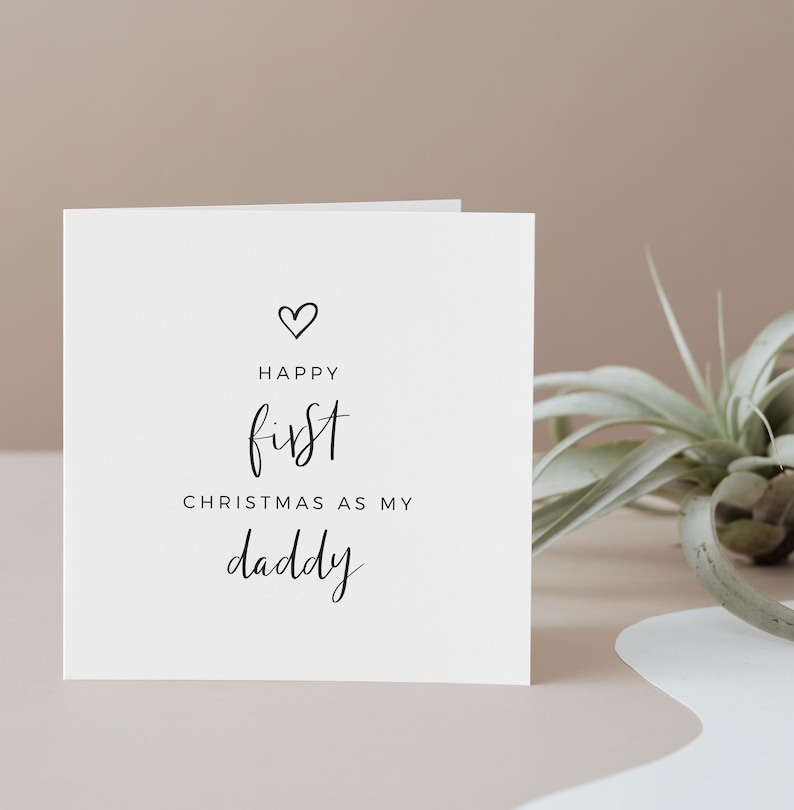 May include: A white card with black text that reads "Happy first Christmas as my daddy" with a small heart symbol above the word "Happy".